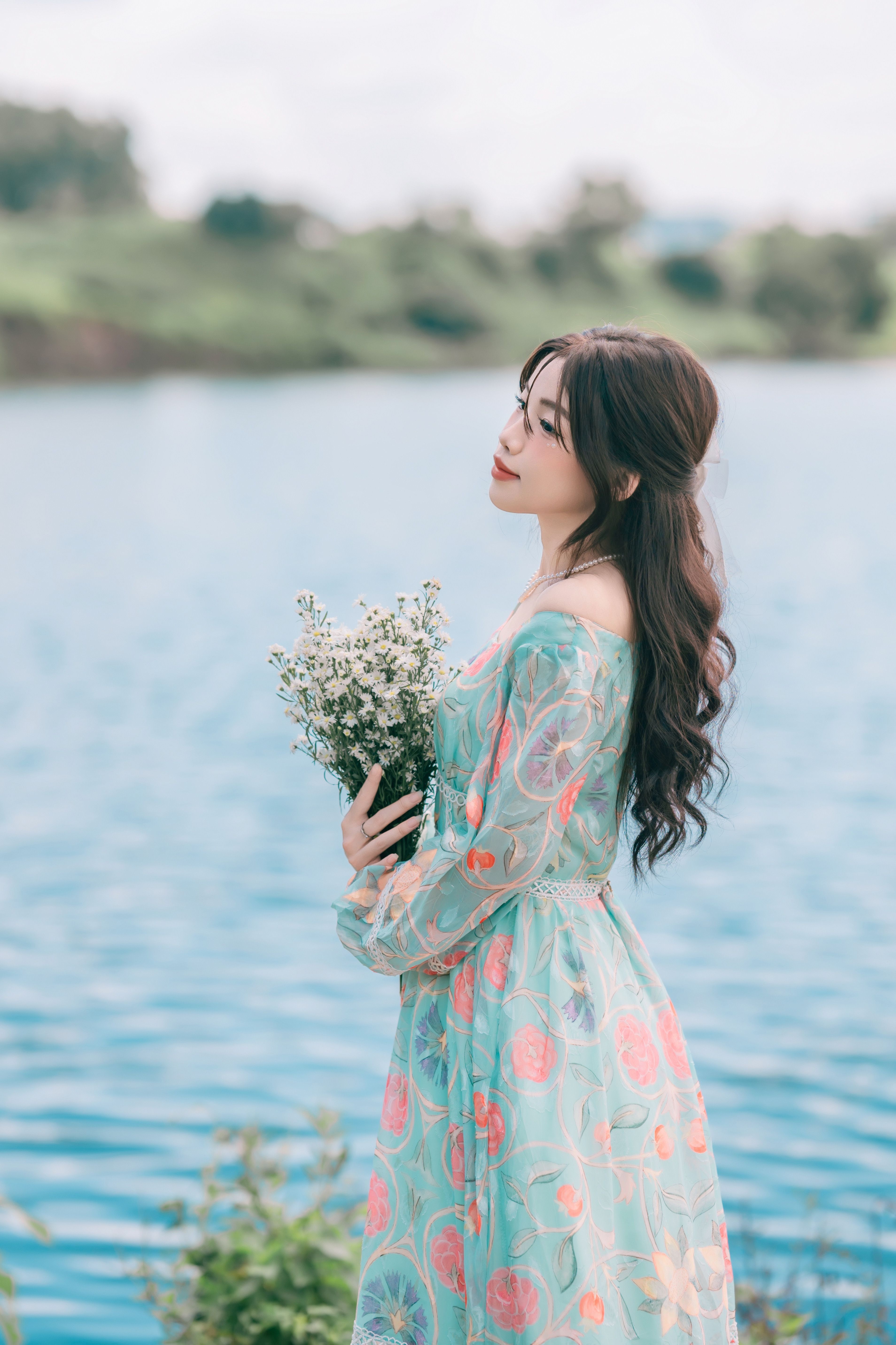 Woman in Floral Dress Holding Flowers by a Lake · Free Stock Photo