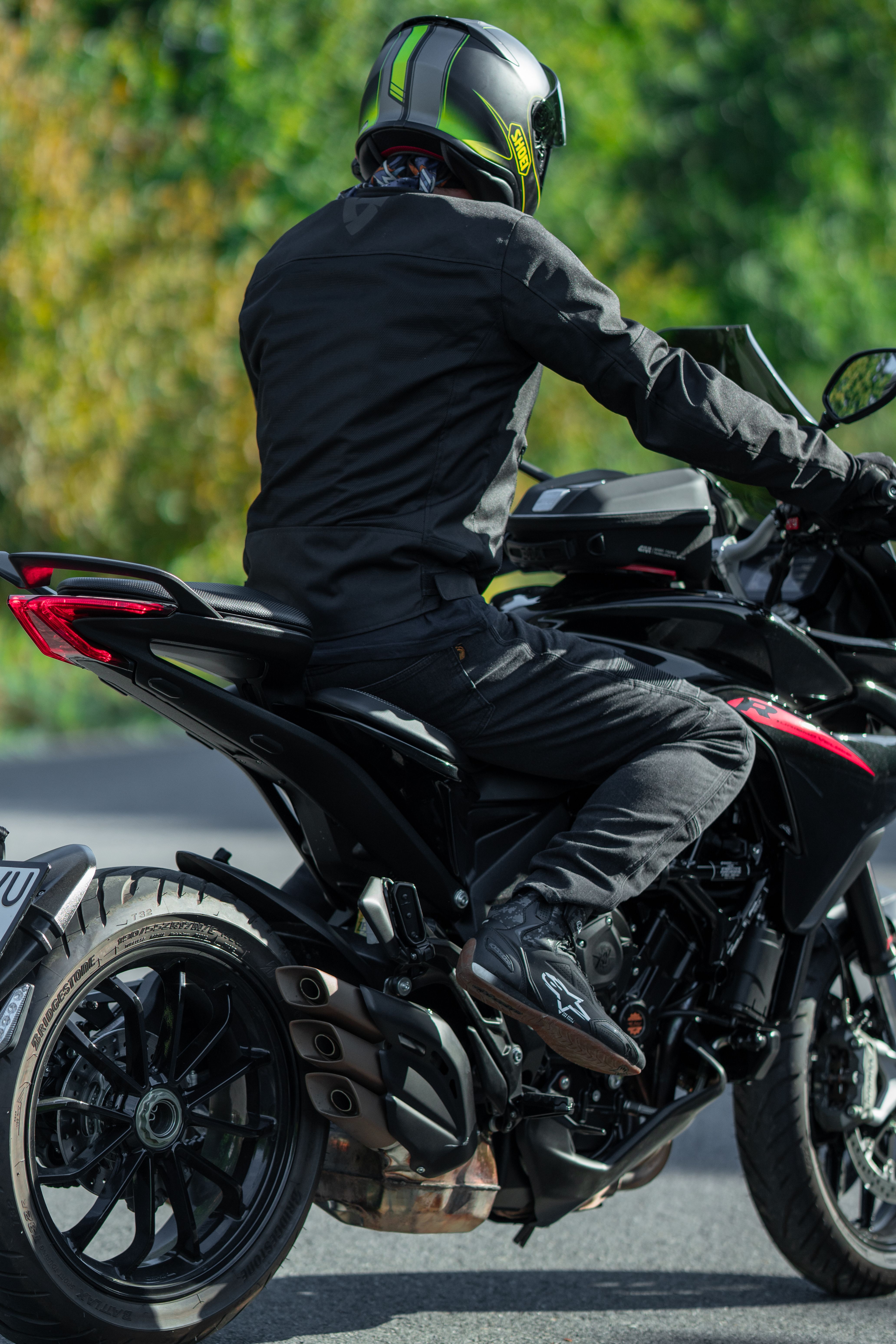 A person in black gear riding a sleek black sports motorcycle on a road.