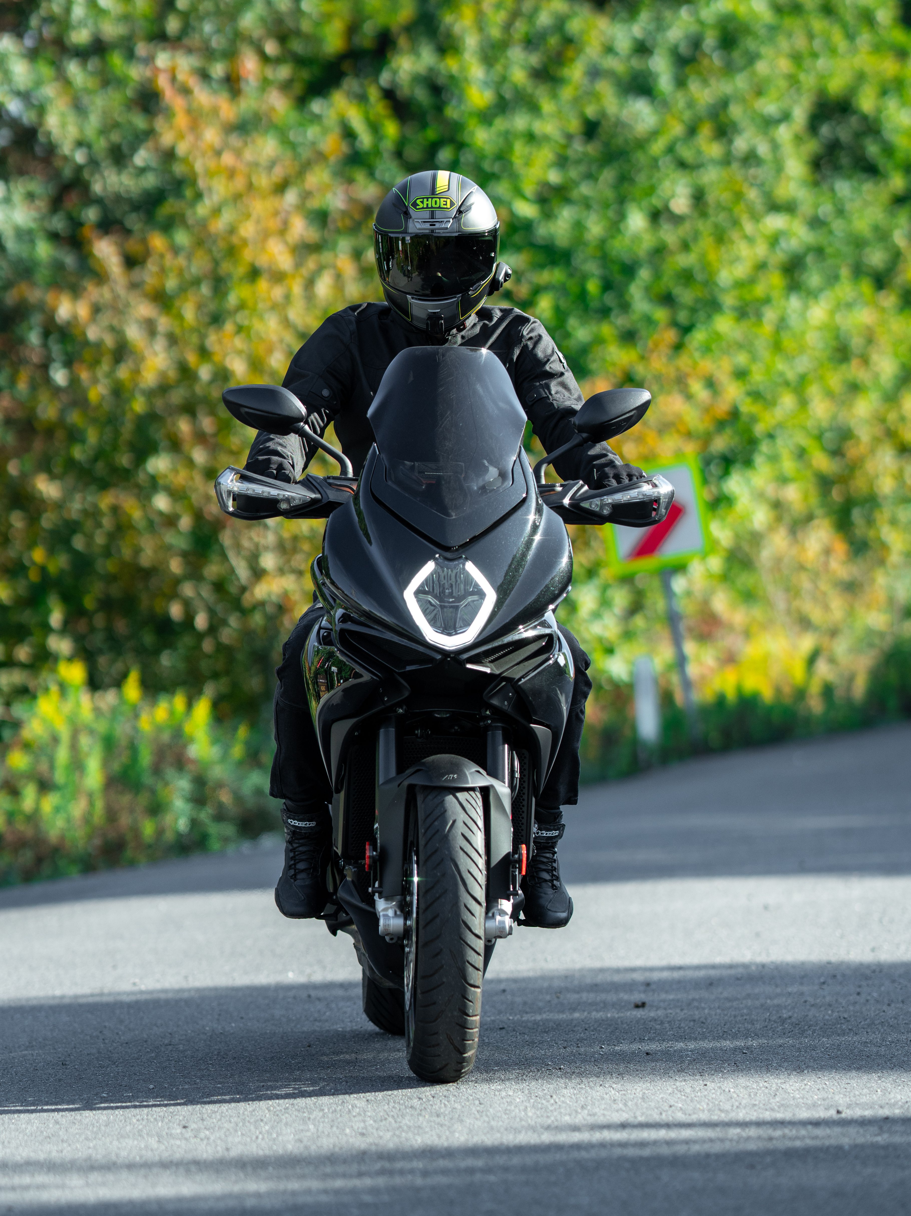 Motorcyclist in full gear rides through lush green scenery on a curvy road.