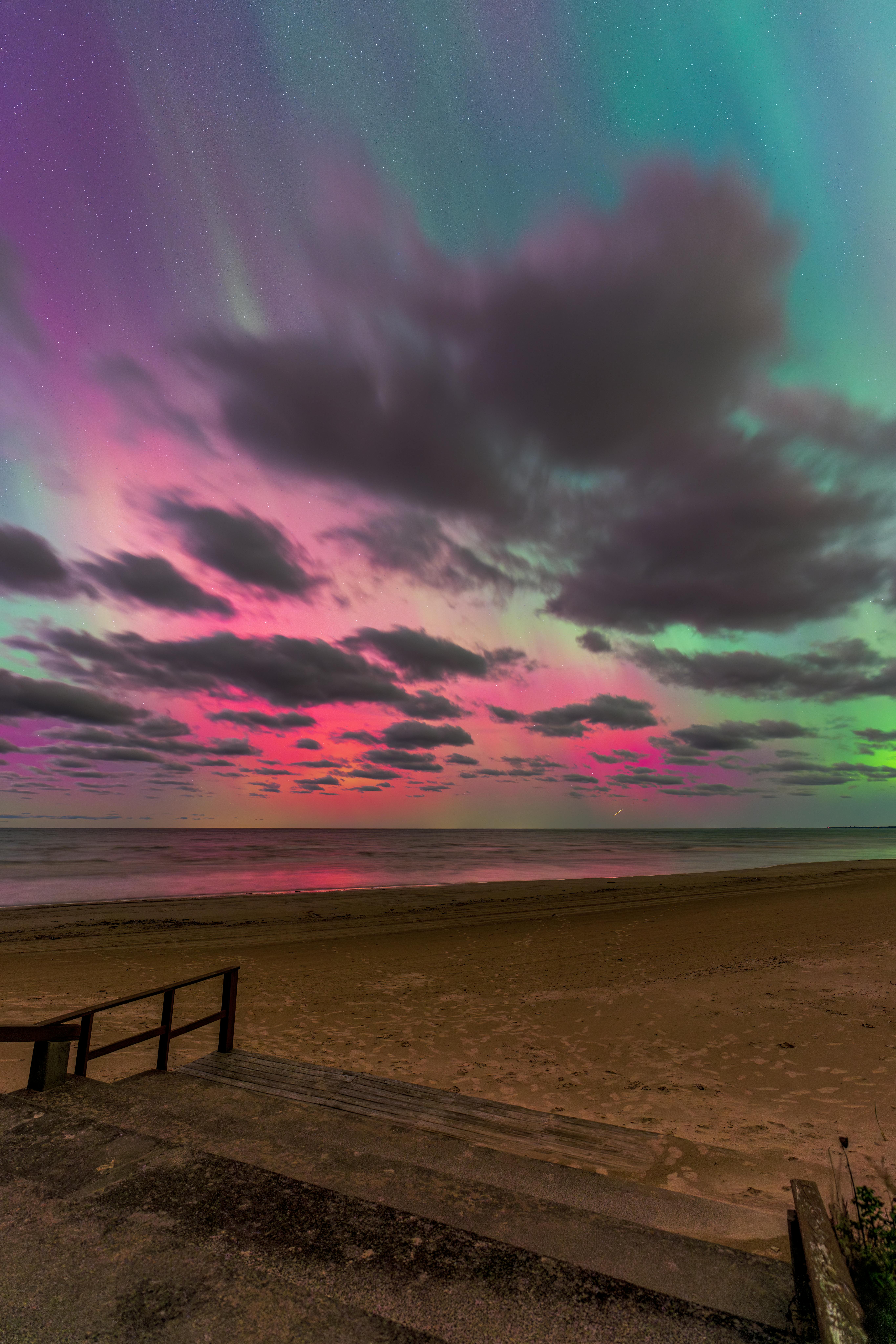 Mesmerizing aurora borealis colors dance over a tranquil beach at twilight.