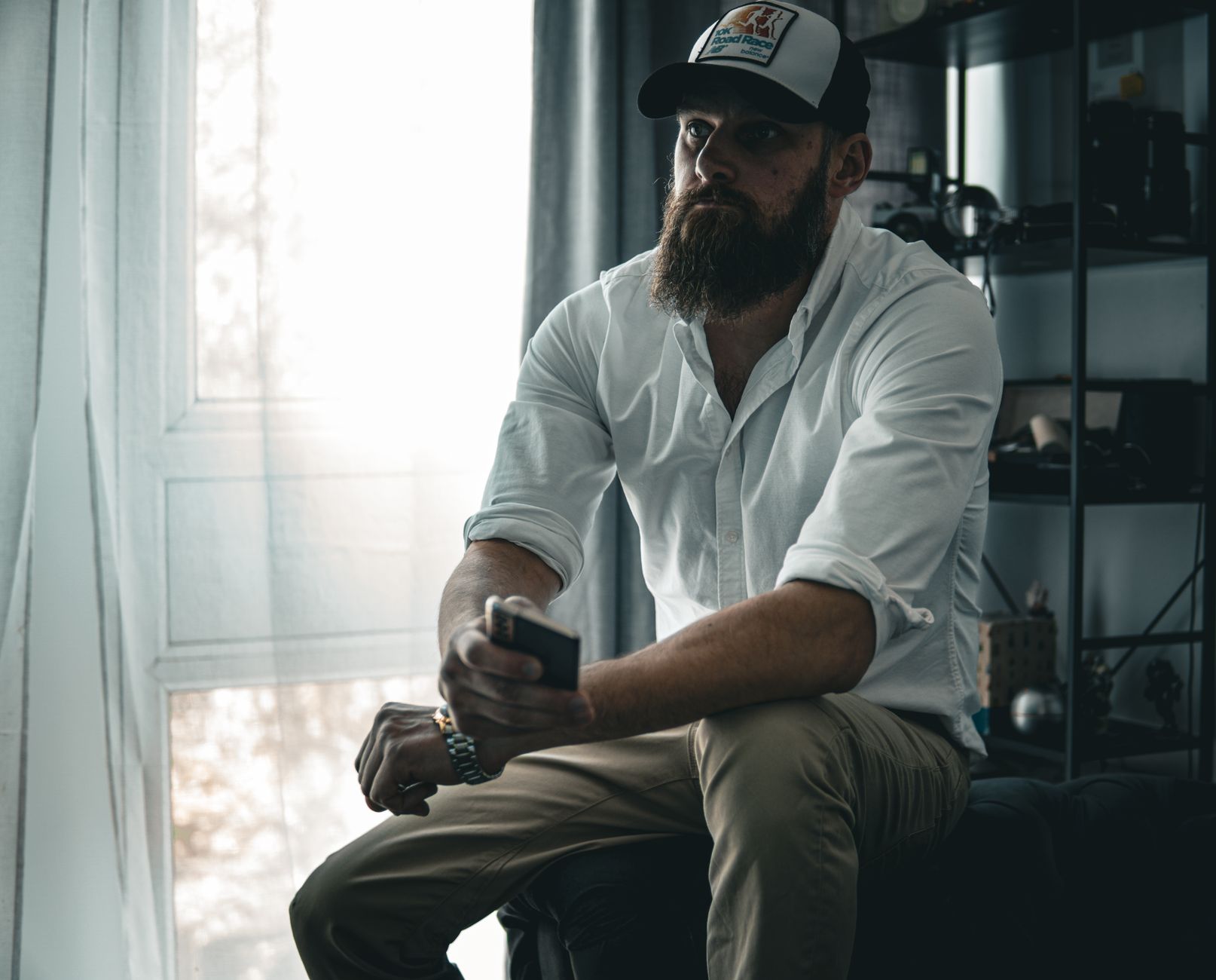 Bearded man in a cap and white shirt sitting thoughtfully in a cozy room.