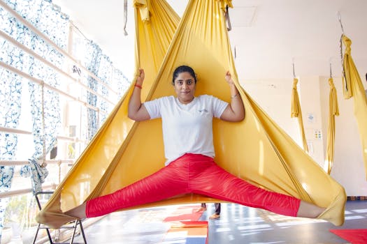 Woman practicing aerial yoga in a sunlit studio performing impressive split pose with fabric hammocks.
