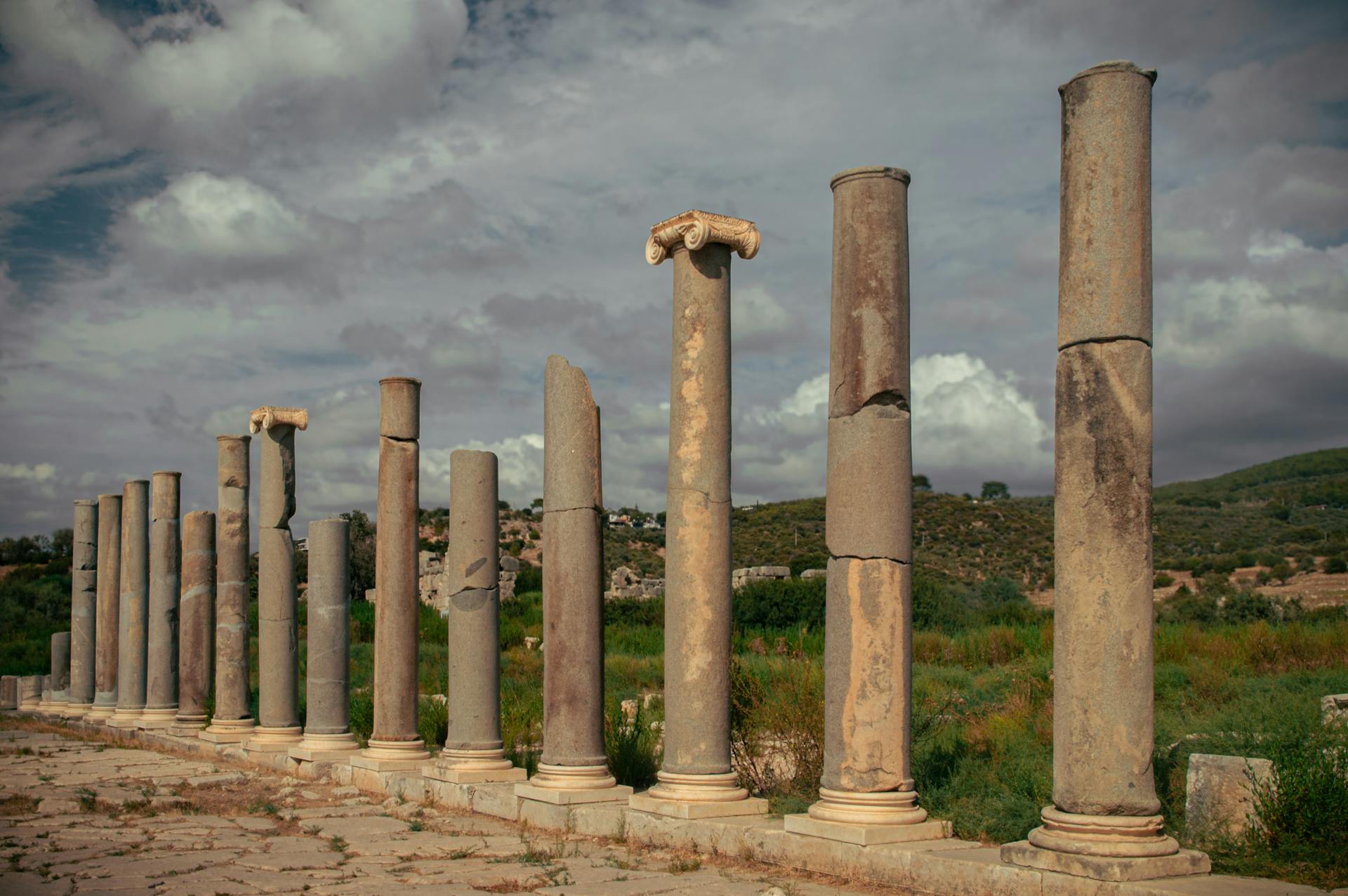 Historic Roman columns by a field under dramatic cloudy sky.