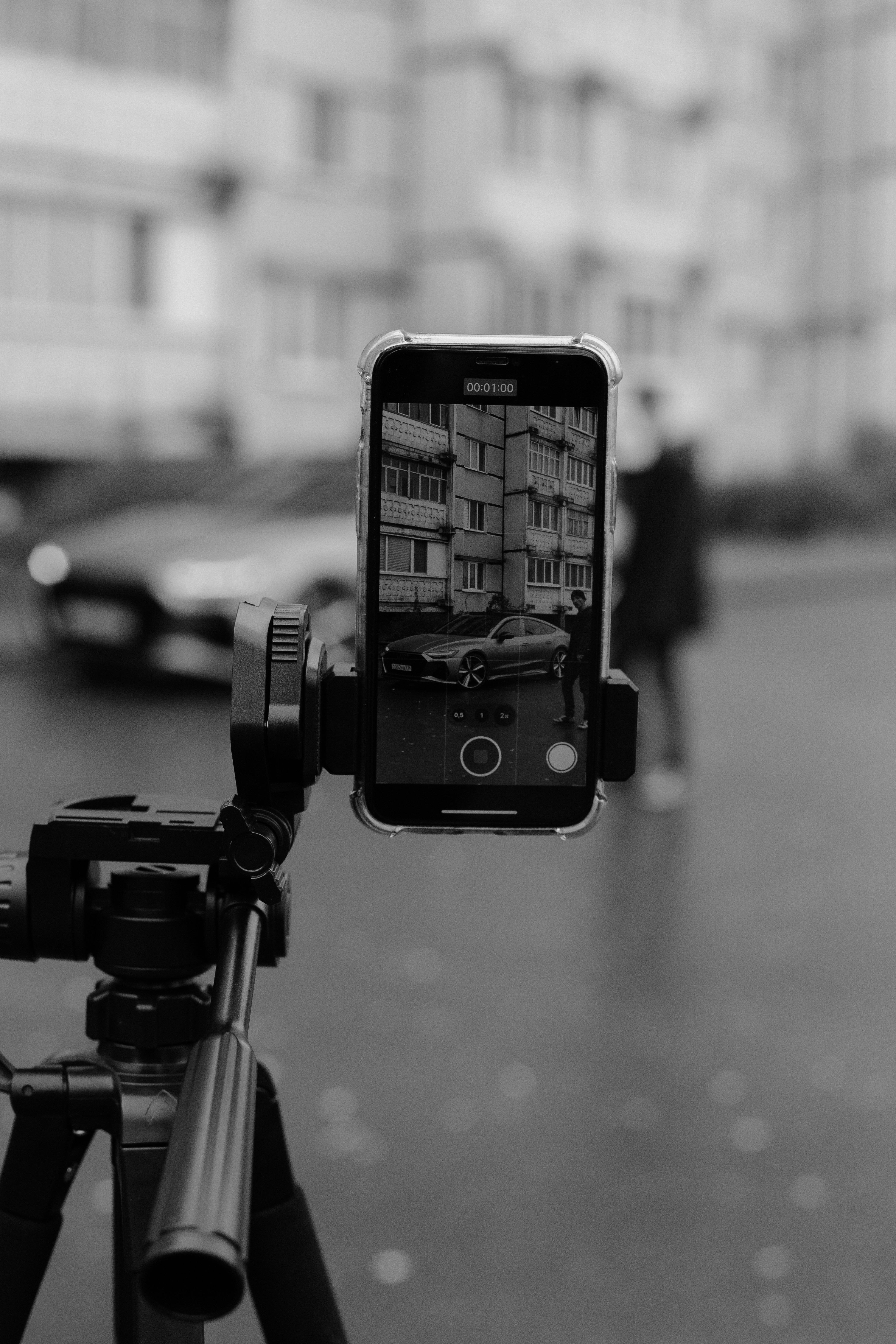 Free Black and white photo capturing a city scene through a smartphone on a tripod. Stock Photo