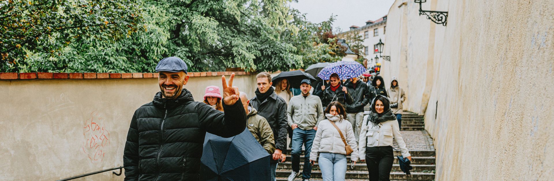 Group of tourists with umbrellas walking down a charming European street during a rainy day.