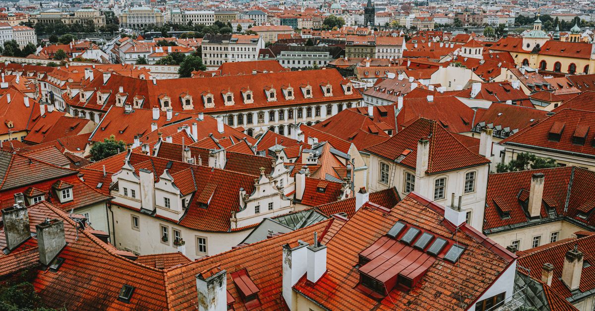 Aerial view over Prague's iconic red rooftops, showcasing traditional architecture and a city skyline.