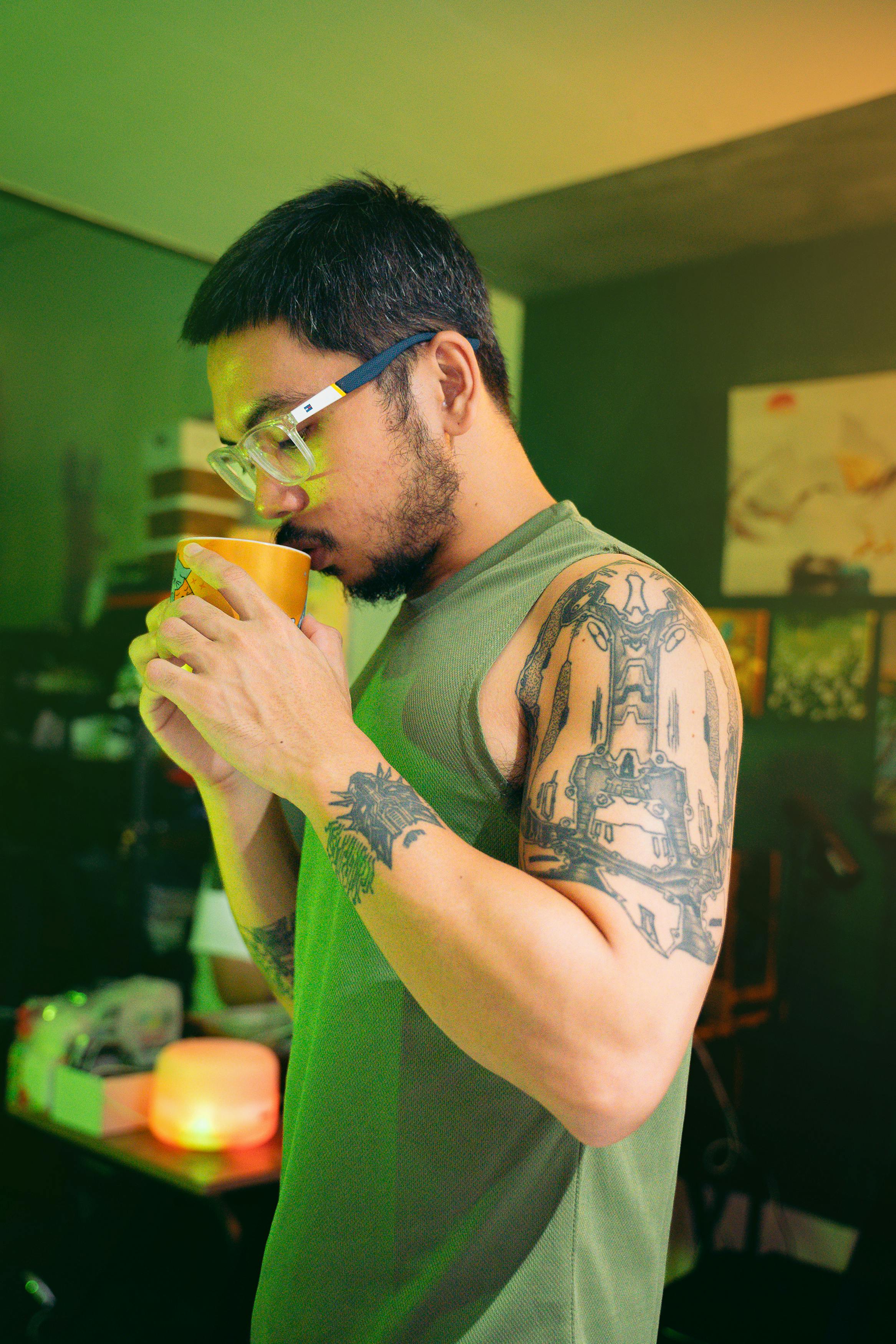 Man with tattoos enjoying a hot beverage in a cozy indoor setting.