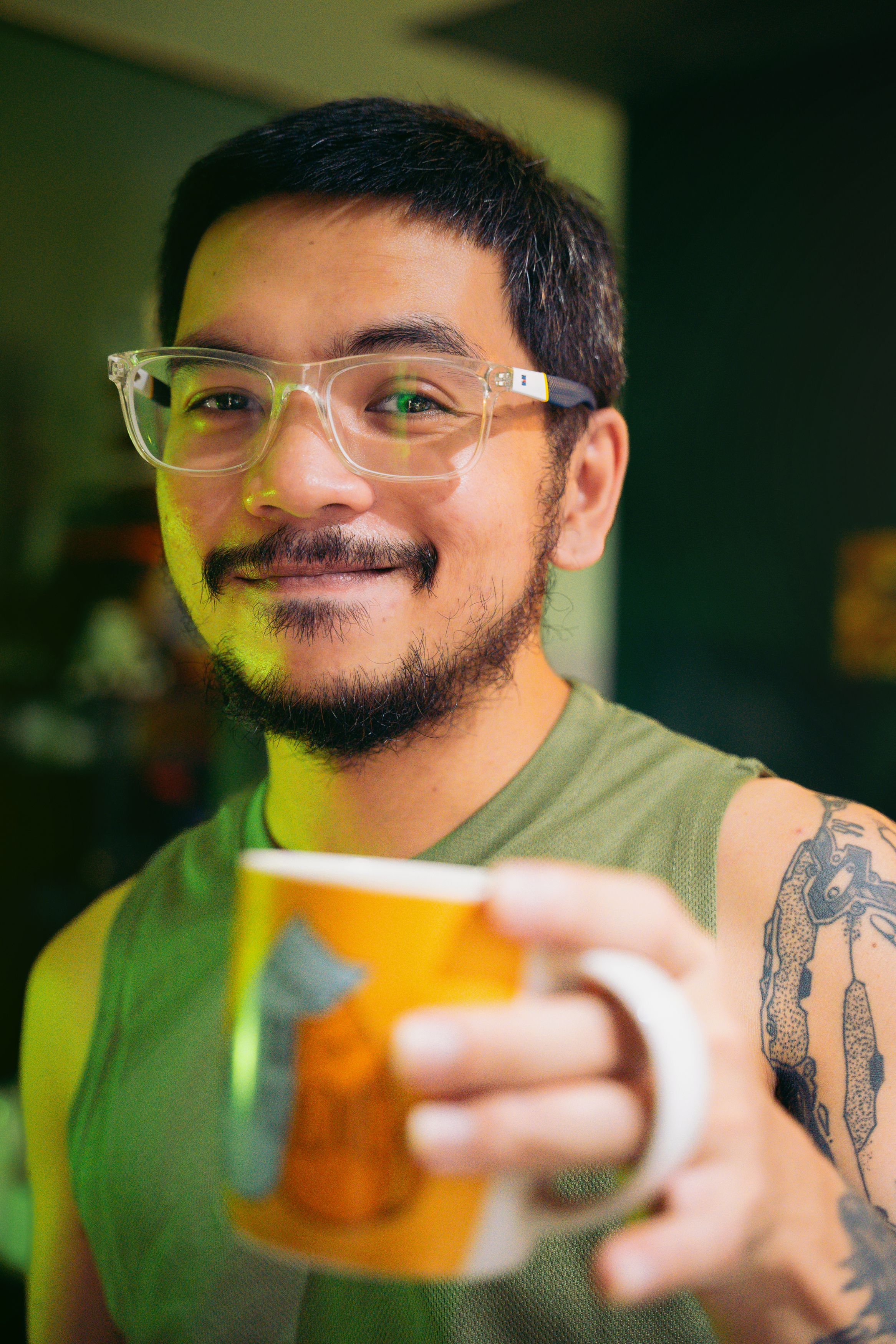 A man with glasses and tattoos holding a mug, enjoying a relaxed moment indoors.
