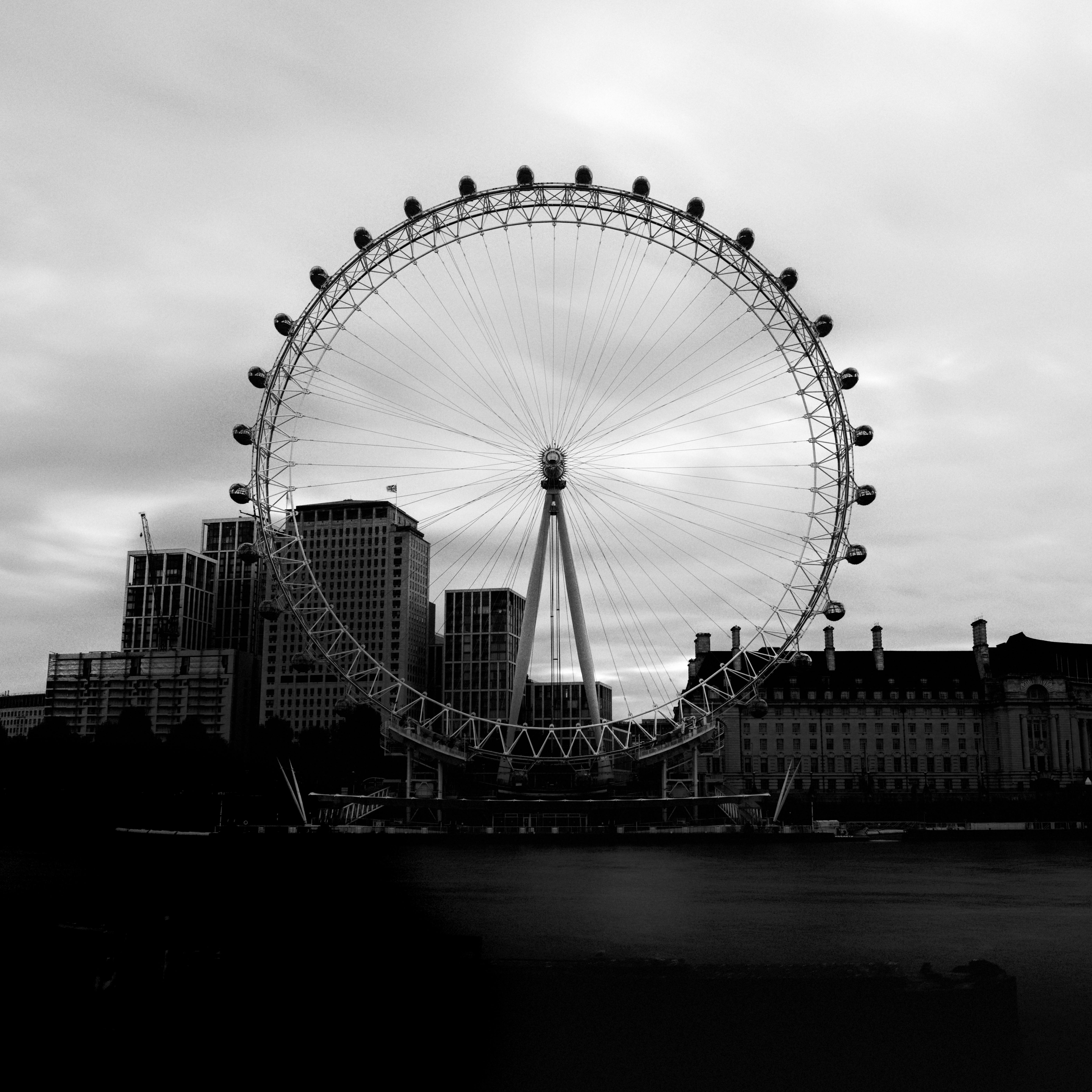 Black and white view of the London Eye over the River Thames, showcasing iconic architecture in England.