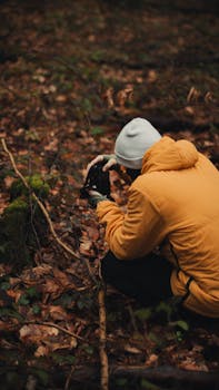 Person in a yellow jacket explores a forest floor filled with autumn leaves.