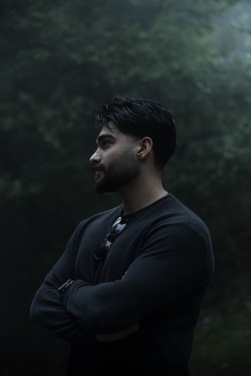 Free Young man stands contemplatively in a misty forest, arms crossed. Stock Photo