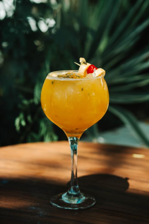 Free Chilled tropical cocktail with fruit garnish on a sunlit wooden table, perfect for summer vibes. Stock Photo