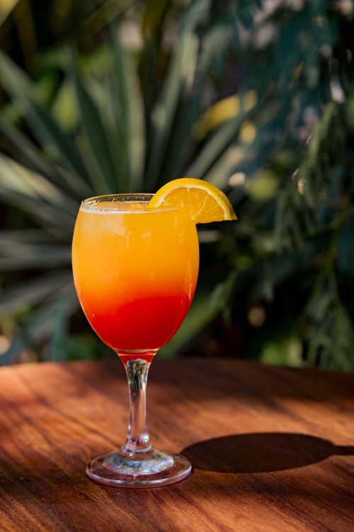 Free Vibrant cocktail with orange slice on a wooden table in a sunny outdoor setting. Stock Photo