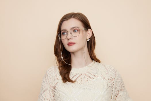Portrait of a woman in a patterned white sweater wearing stylish eyeglasses against a neutral background.