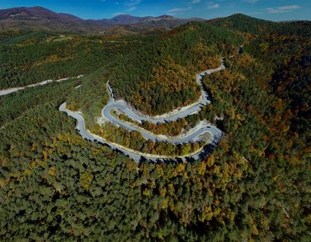 Aerial shot of a winding serpentine road through a green forest in France.