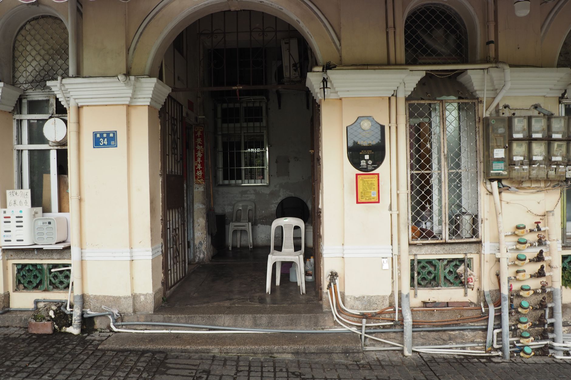 View of the front entrance of an old residential building with chairs and utility meters.