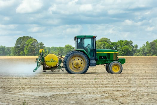 一辆绿色的喷雾拖拉机在多云天空下的开阔农田里工作