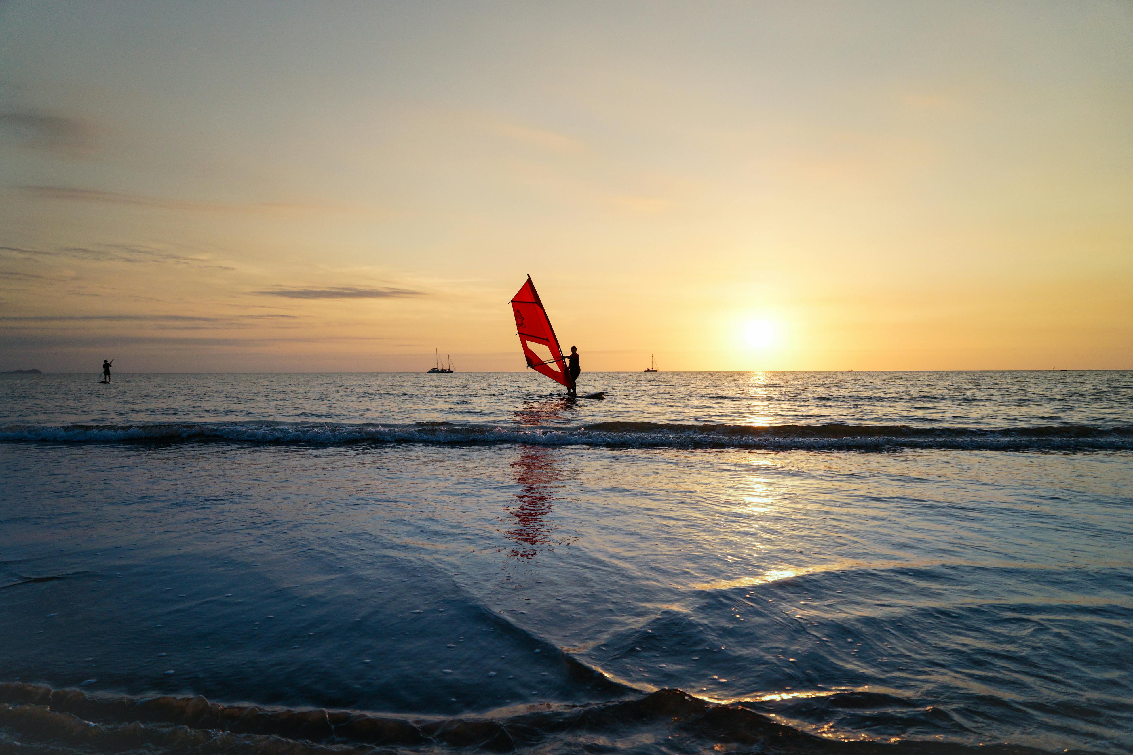 A wind surfer sails at sunset in the open sea, casting a silhouette against the horizon.