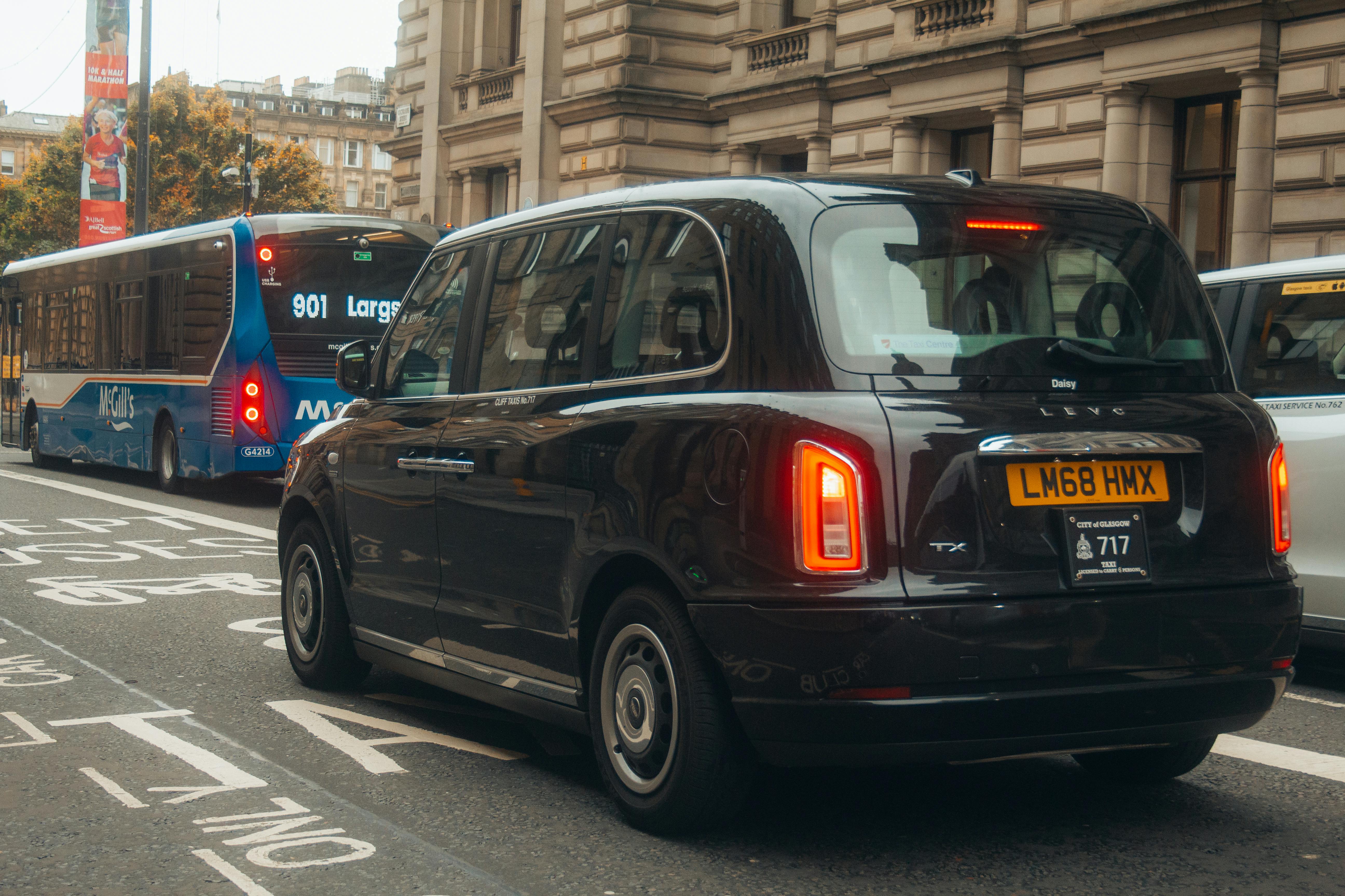 Classic black taxi cab on a city street in Glasgow with buses and a historic building.