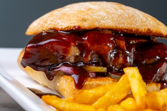 Ciabatta sandwich oozing glossy barbecue-glazed pork, pickles and red onion with fries