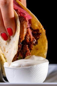 Hand holding a taco dipped in sauce—explore Mexican flavors.