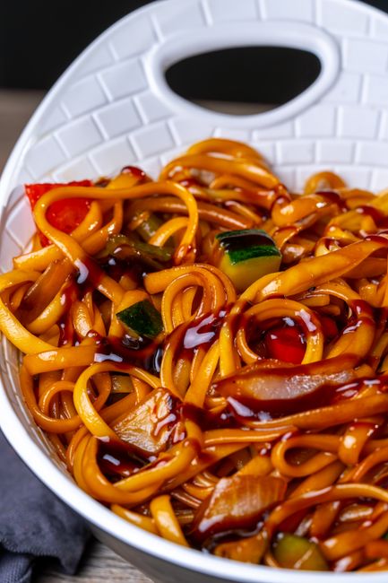 A small ceramic bowl of dark glossy hoisin sauce next to a wok of stir-fried vegetables and a spoon resting on the counter
