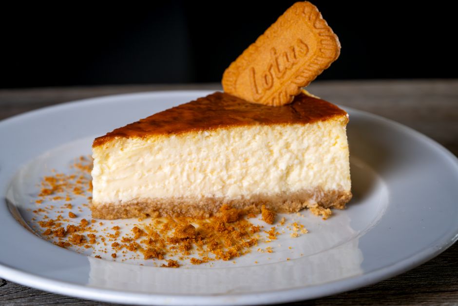 Creamy cheesecake slice topped with a Lotus biscuit on a white plate.