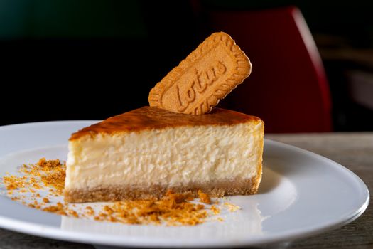 Slice of cheesecake topped with a Lotus Biscoff cookie on a white plate.