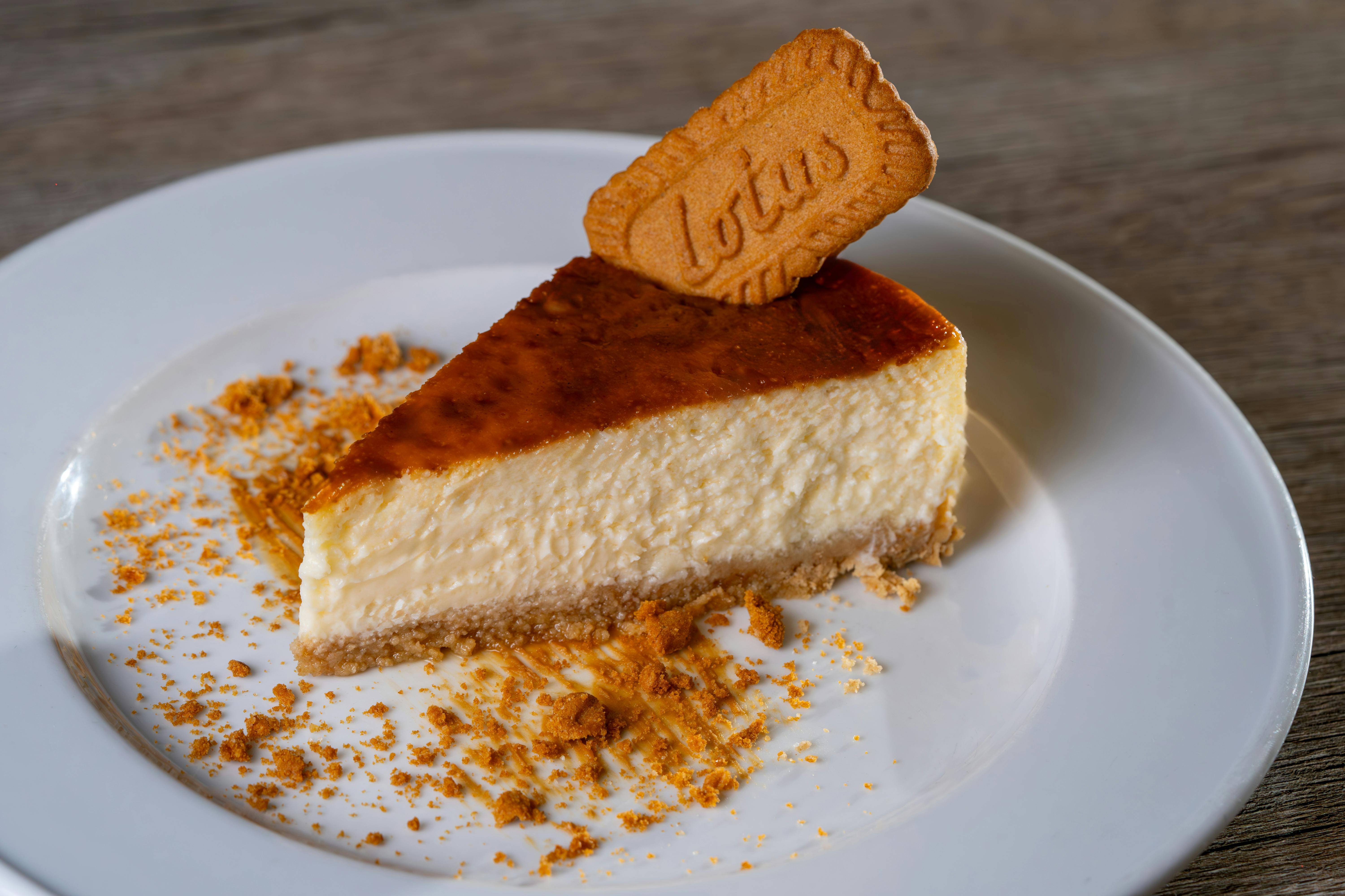 Creamy cheesecake slice topped with a Lotus biscuit on a white plate.