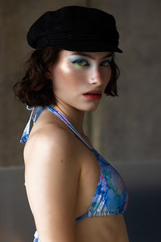 Stylish woman in colorful makeup and hat posing indoors.