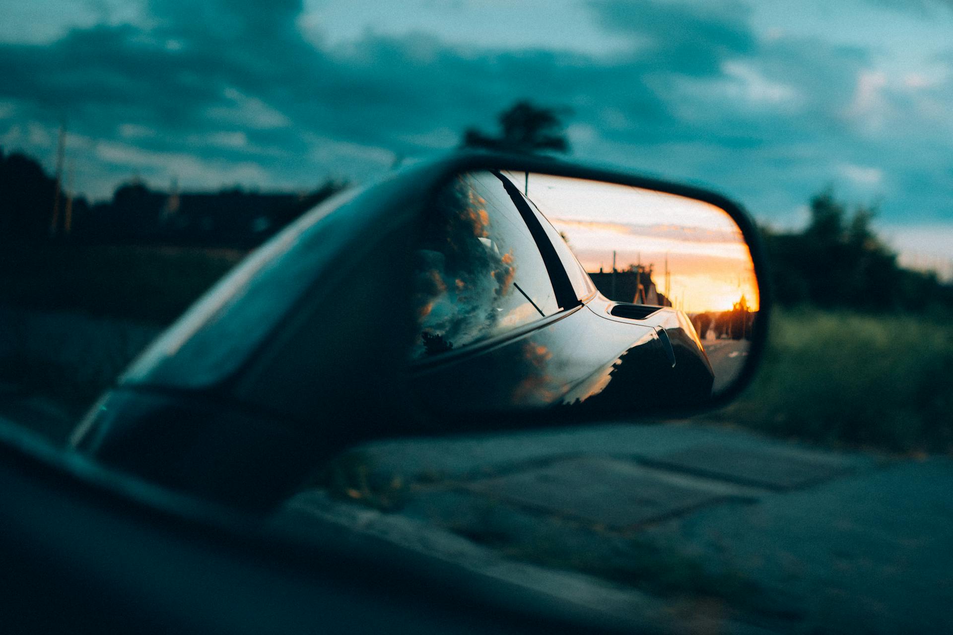 A car side mirror captures a stunning sunset with vivid skies and road reflection.