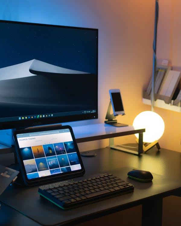Free Sleek indoor workspace featuring computer, tablet, glowing desk lamp, and modern décor. Stock Photo