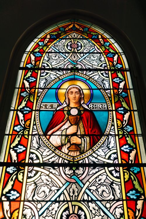 Free Vibrant stained glass window featuring Saint Barbara with detailed religious iconography. Stock Photo