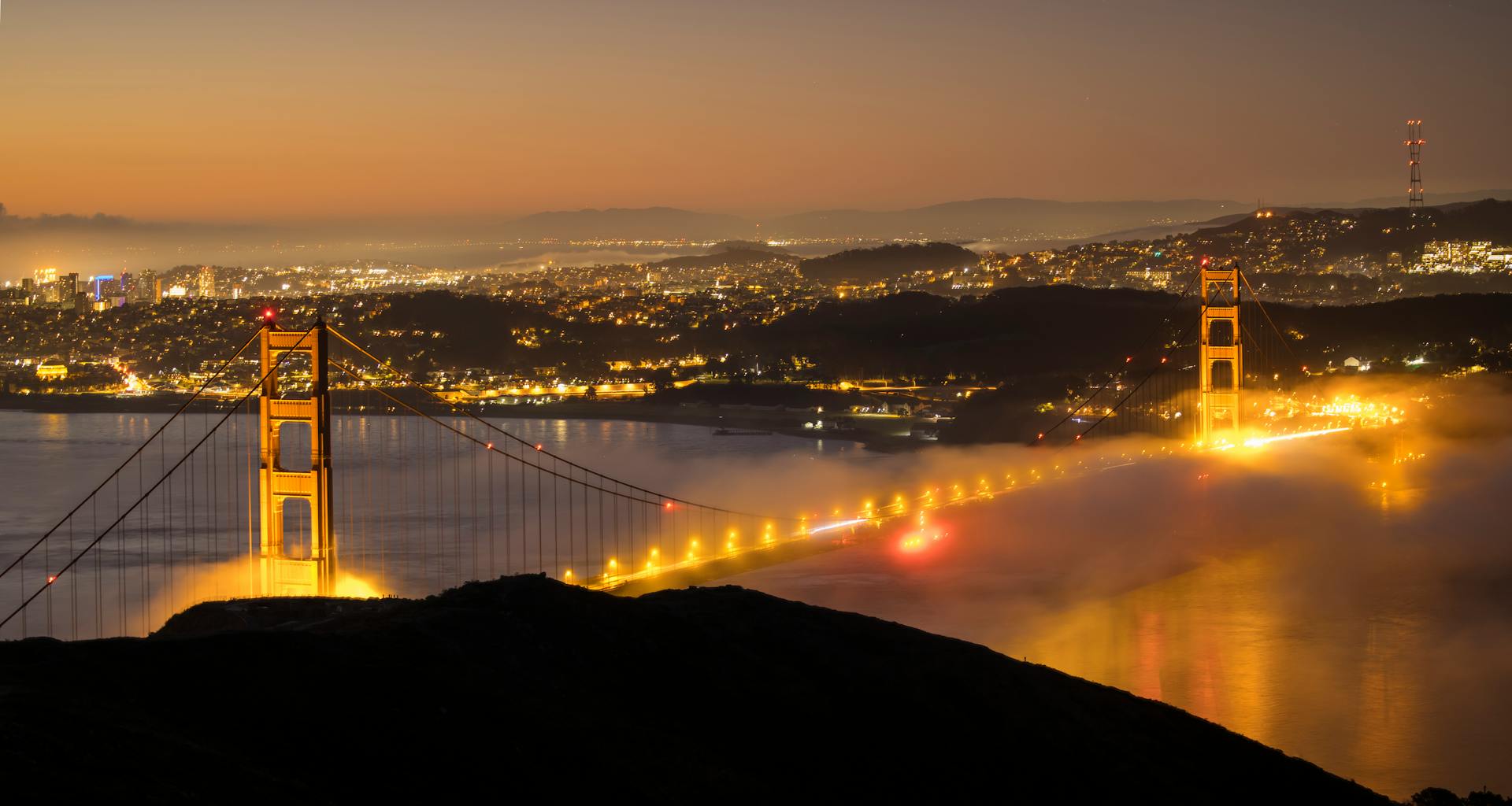 Stunning view of the Golden Gate Bridge illuminated at night amidst San Francisco city lights and mist.