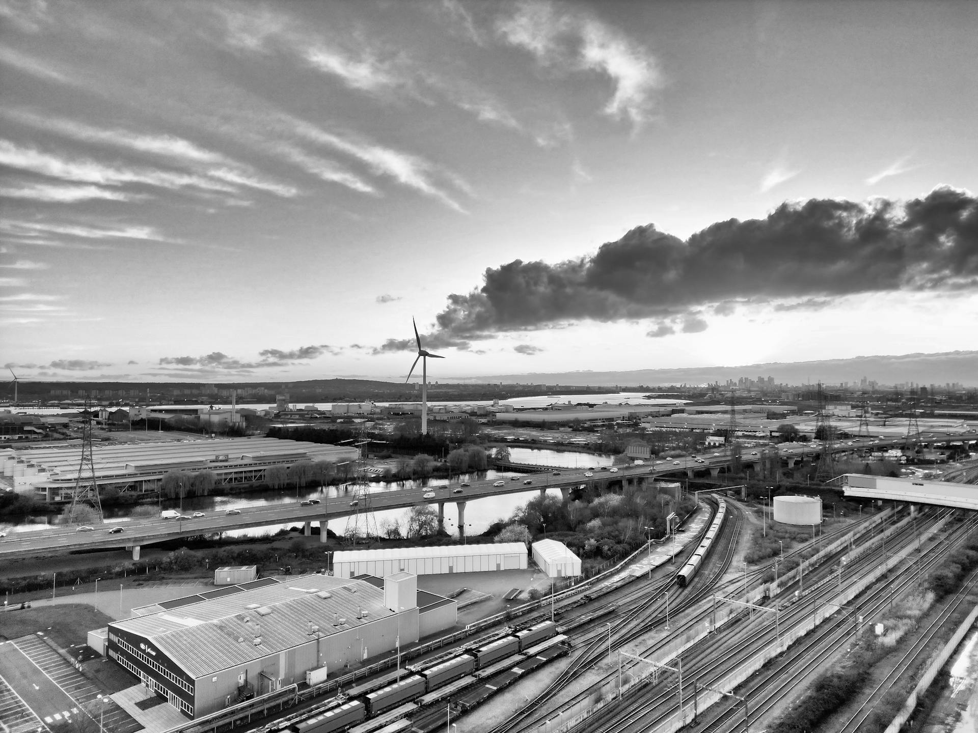 Black and white aerial view of an industrial area with a wind turbine and railway tracks near London.