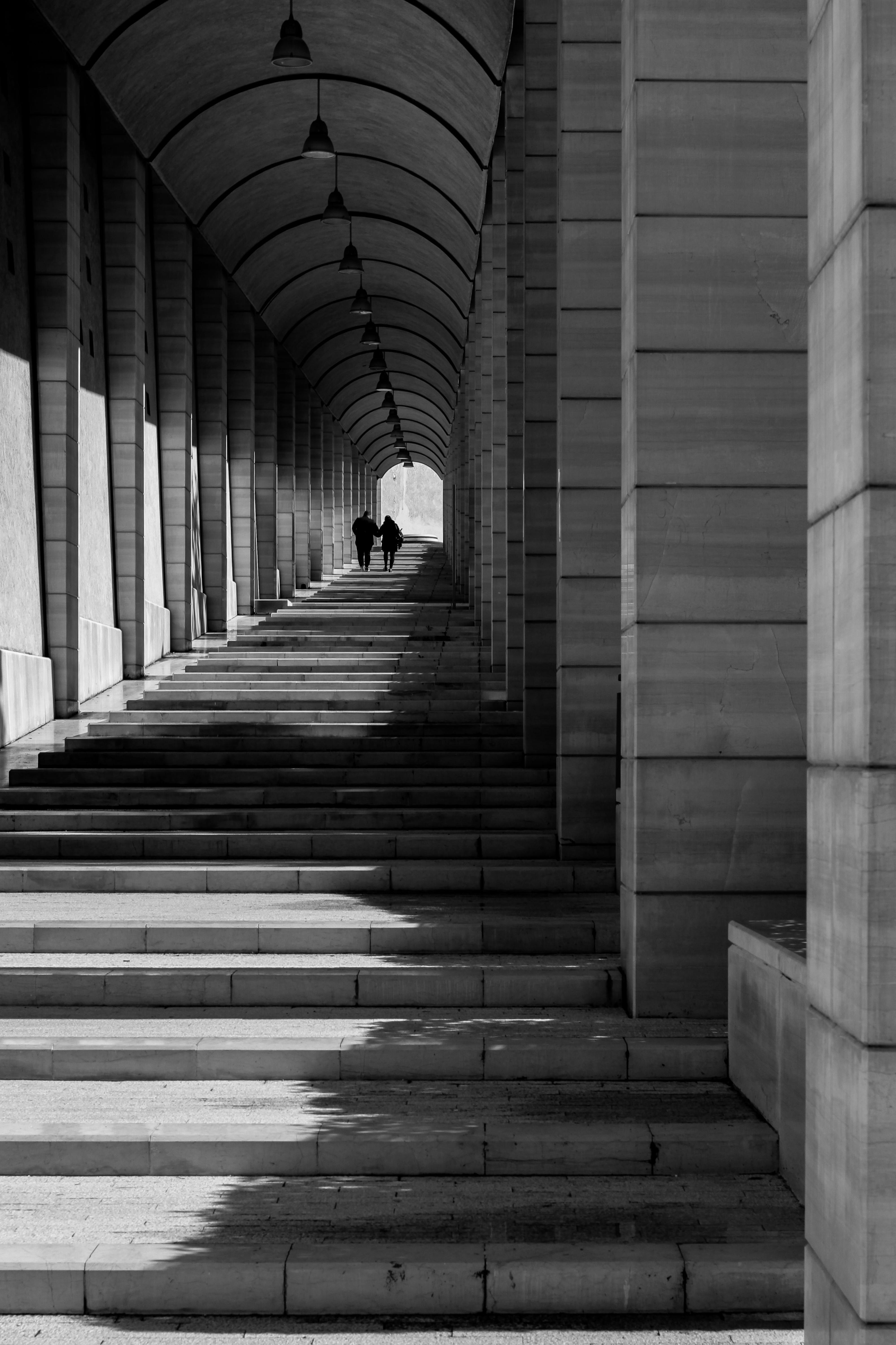 Monochrome scene of a couple walking through a grand archway in an urban setting.
