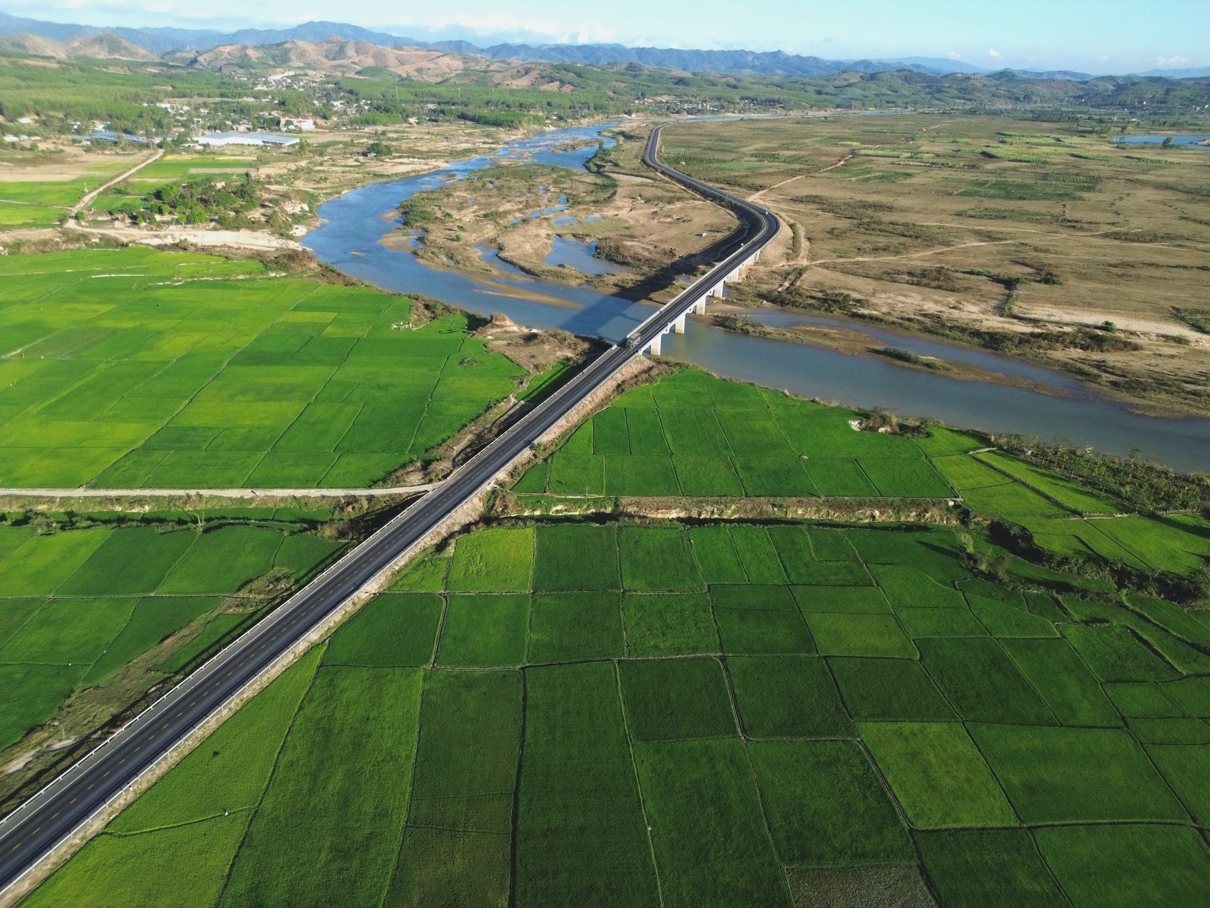 Aerial view of green rice fields, river, and bridge in Kon Tum, Vietnam.