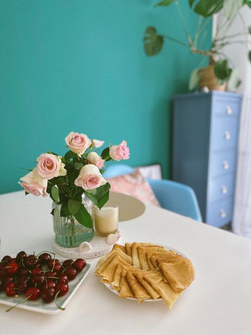Free A cozy breakfast scene with pancakes, cherries, and pink roses on a white table. Stock Photo