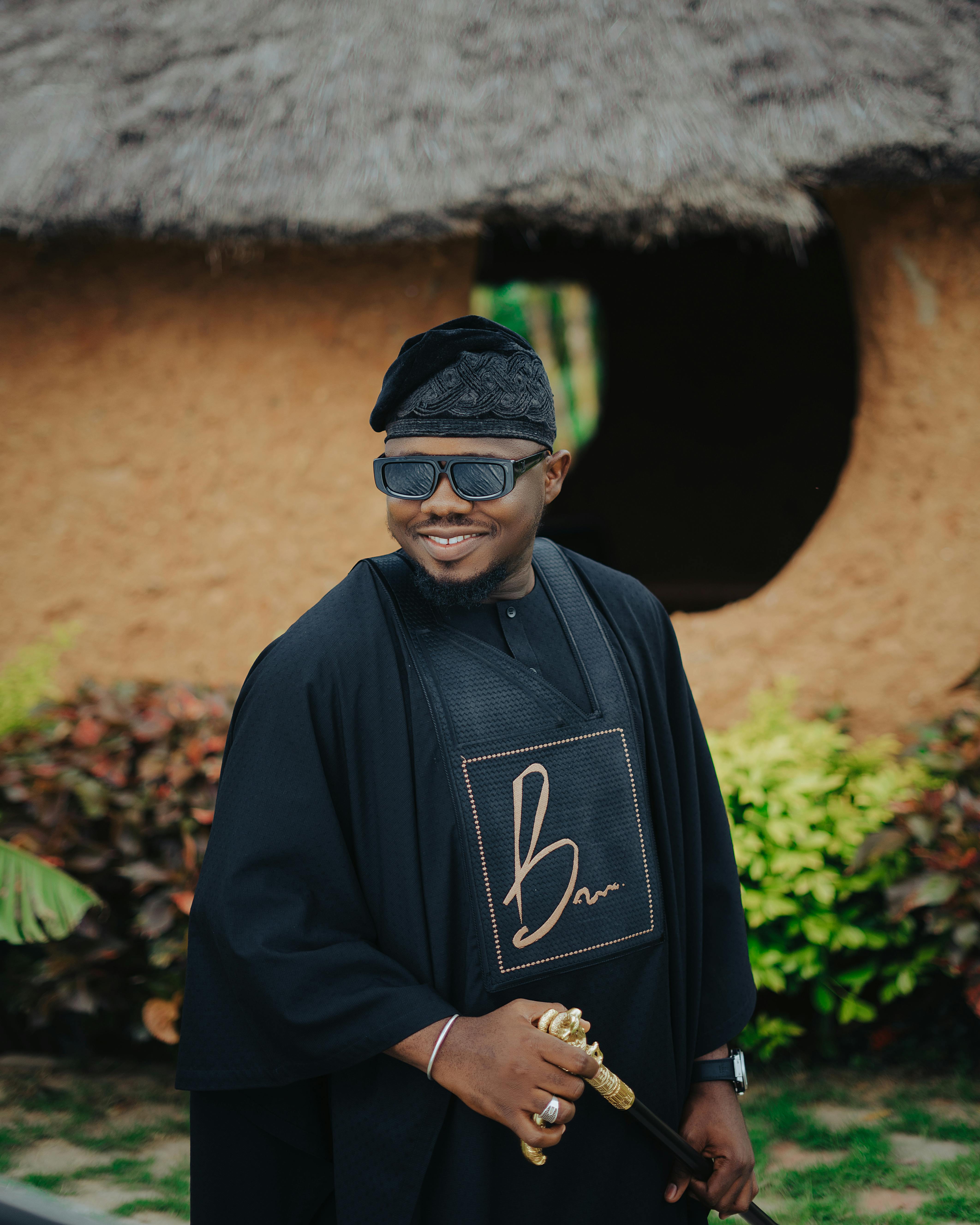 Man in traditional Nigerian attire with modern accessories, standing outdoors.