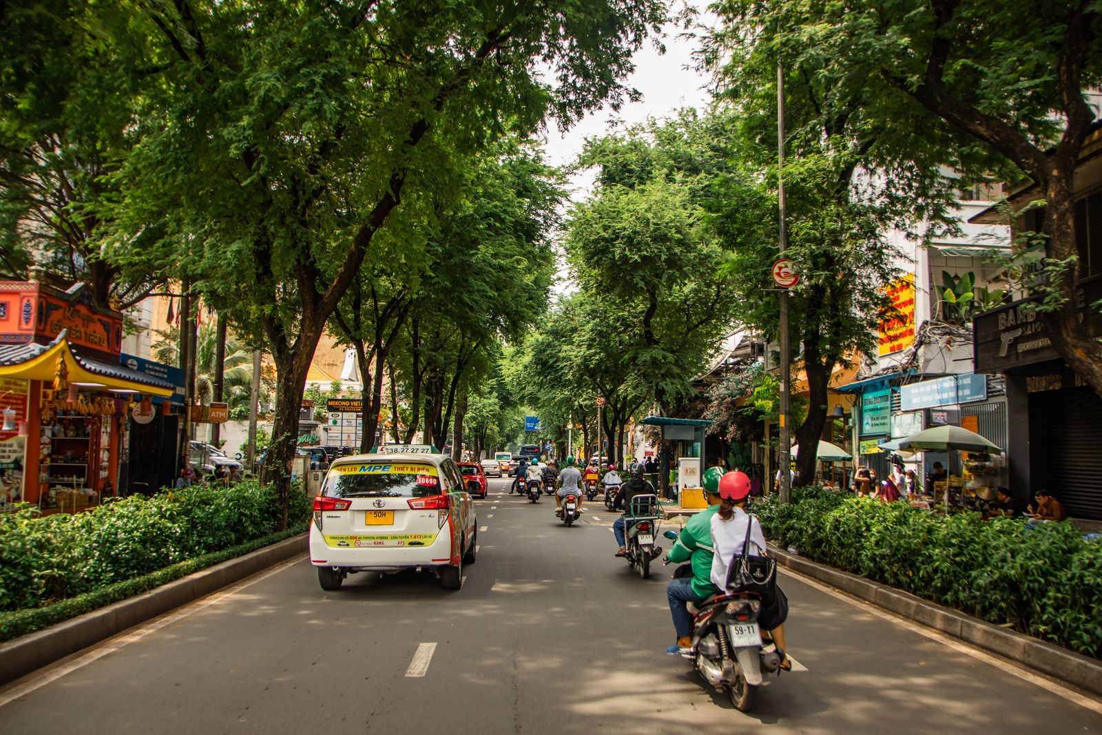 Mid-morning traffic under the street trees in central Ho Chi Minh City, with taxis and motorbikes