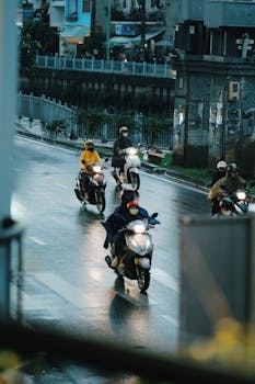 Group of motorcyclists navigating a wet urban road in rainy weather.