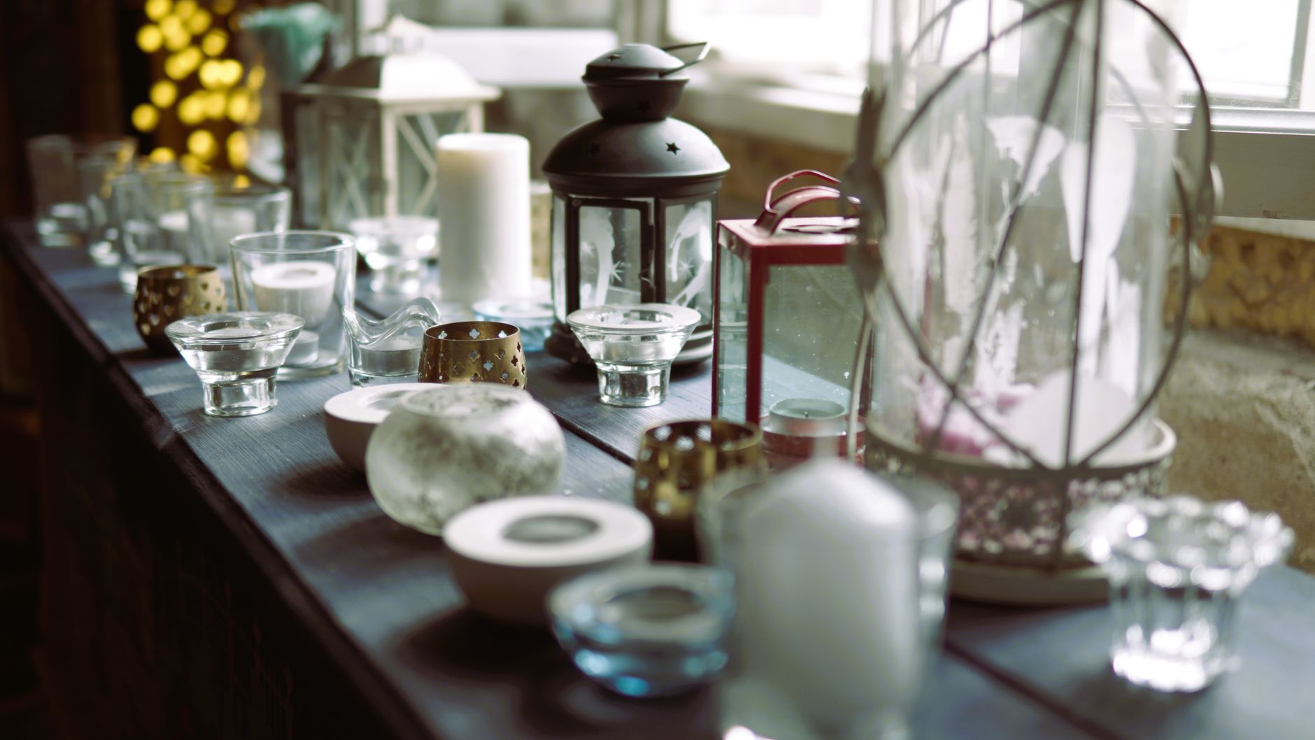 Aesthetic indoor setting with various candles and lanterns on a windowsill, creating a warm ambiance.