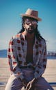 阳光明媚的海滩上，一位时髦的黑人戴着帽子和太阳镜摆着姿势