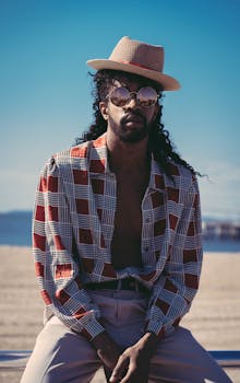 阳光明媚的海滩上，一位时髦的黑人戴着帽子和太阳镜摆着姿势