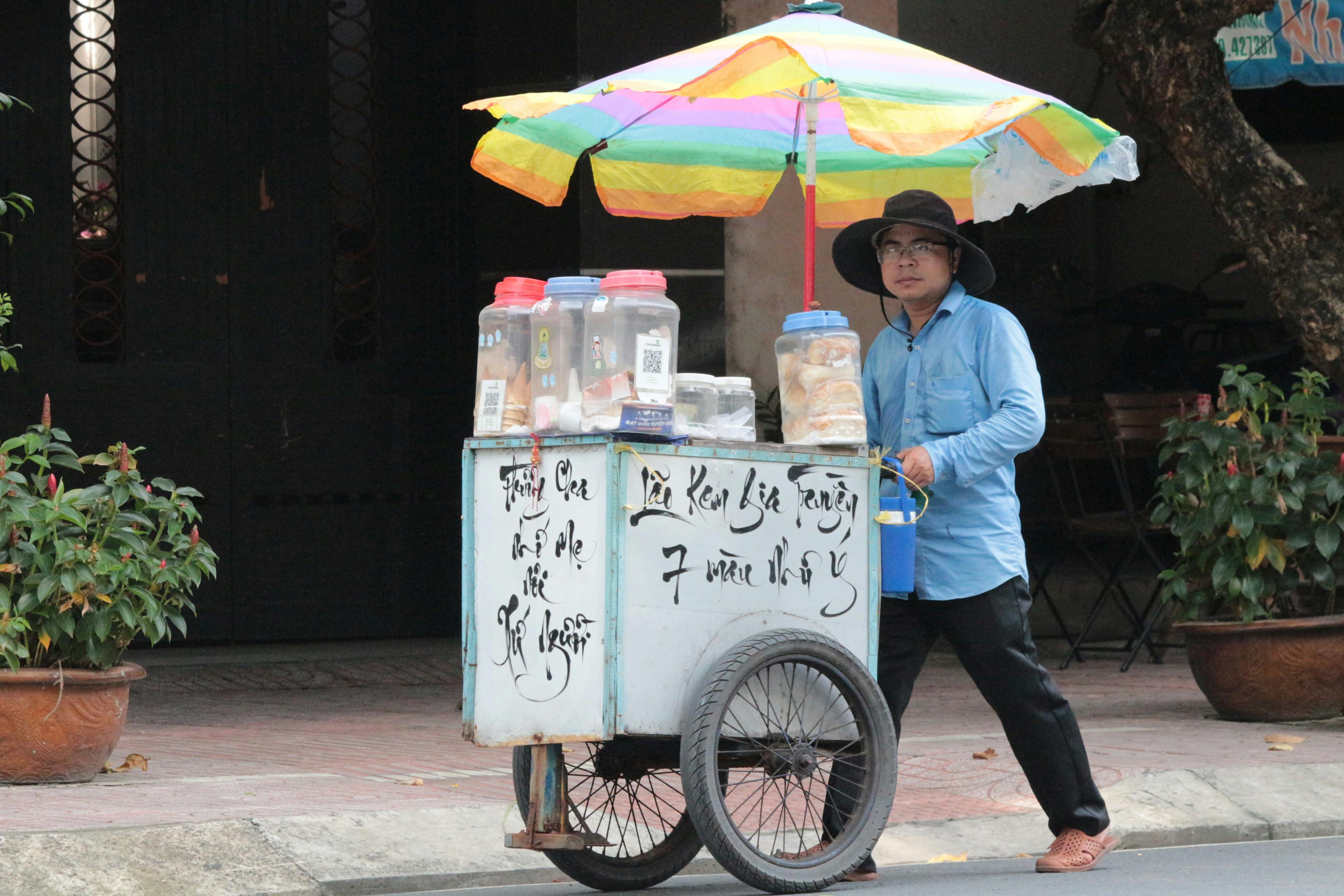 A street vendor pushing an ice cream cart in Ho Chi Minh City, Vietnam, offering a taste of local culture.