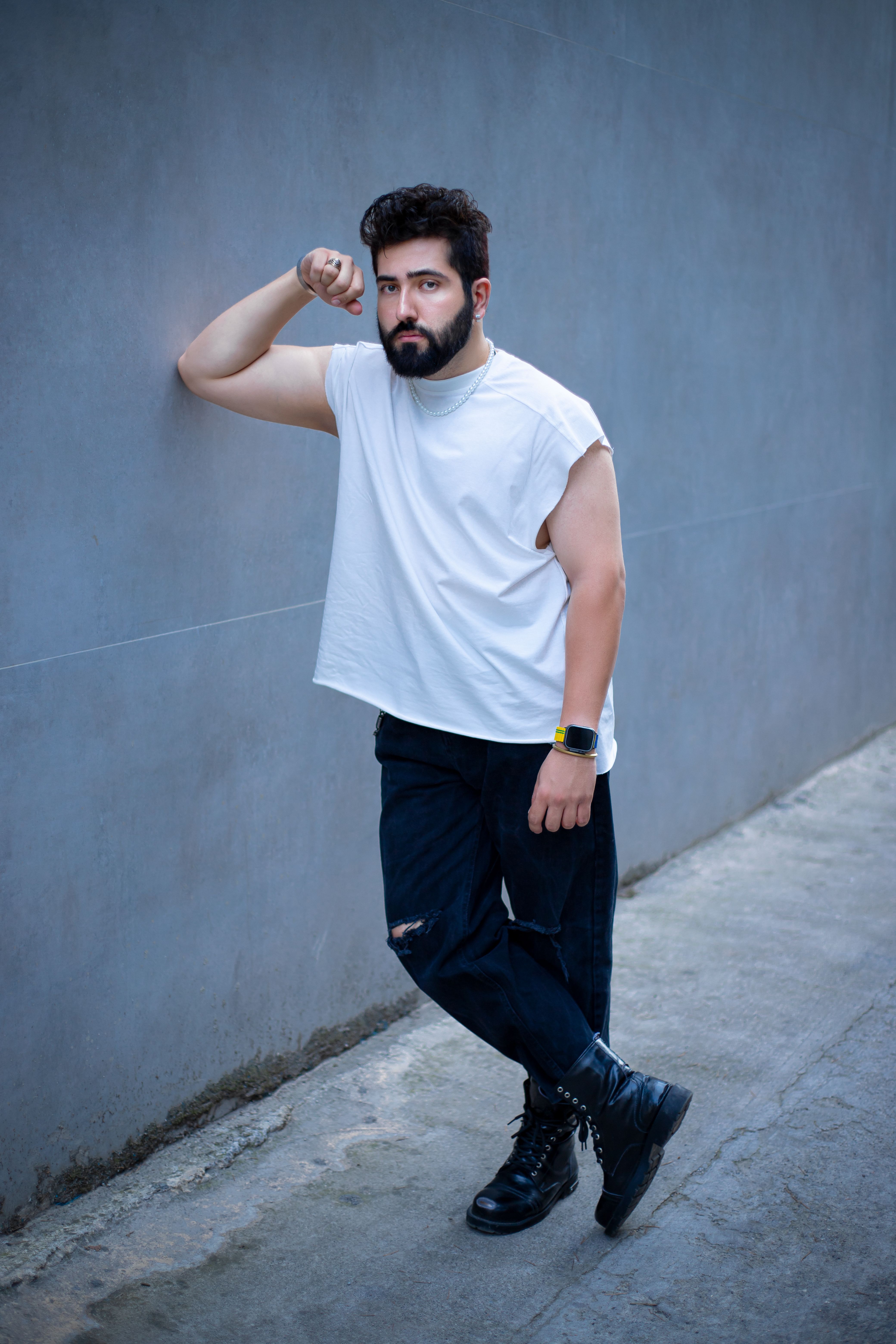 Young man leaning against concrete wall, showcasing casual fashion in an urban setting.