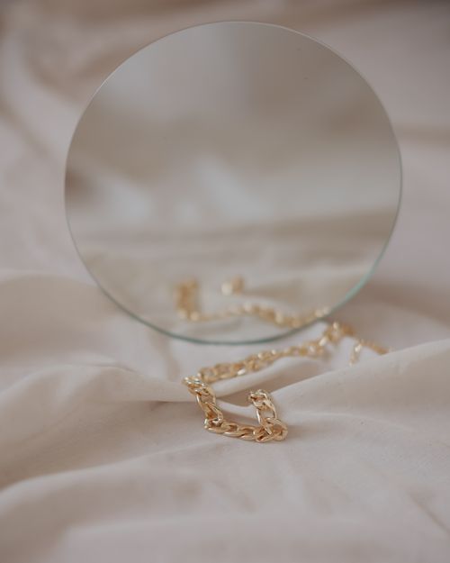 Free A gold chain elegantly displayed on soft fabric with a round mirror reflection. Stock Photo
