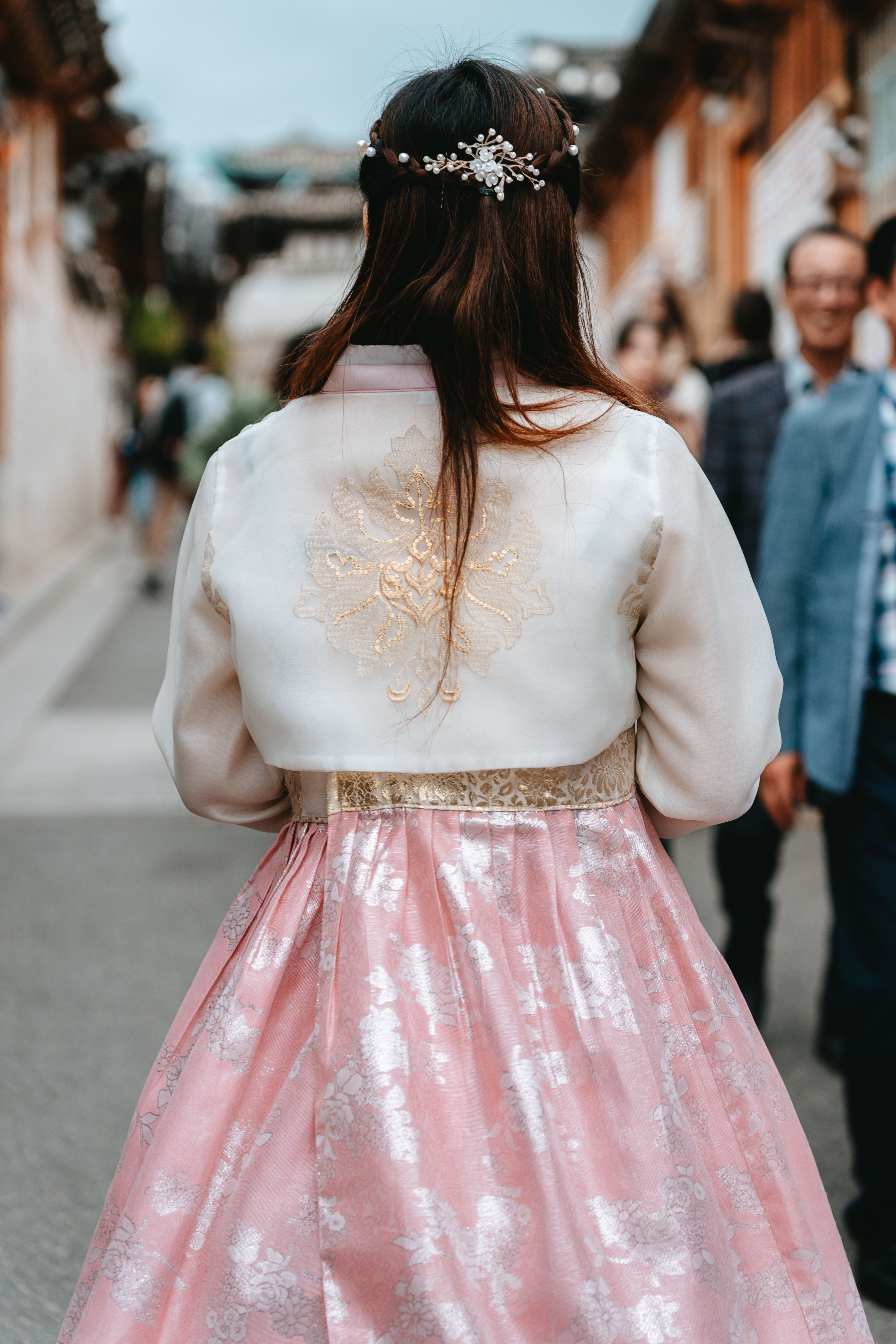 Back view of a woman in a pink traditional hanbok walking in a Seoul street.
