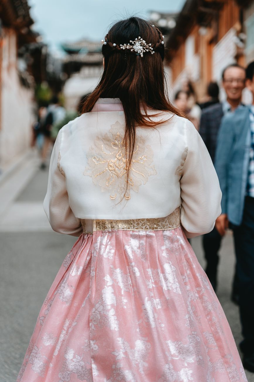Back view of a woman in a pink traditional hanbok walking in a Seoul street.