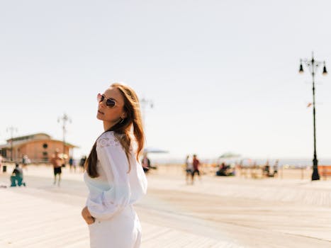 一位时尚女士戴着墨镜，在晴朗的天空下，悠闲地沿着科尼岛木板路漫步